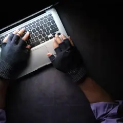 Ręce w rękawiczkach bez palców piszą na laptopie. To może być początek fascynujących studiów kryminalistycznych.