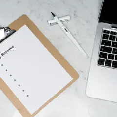 Na biurku leży laptop, białe pióro i kartka z napisem "My Resume". Idealne miejsce do przygotowania CV po angielsku.