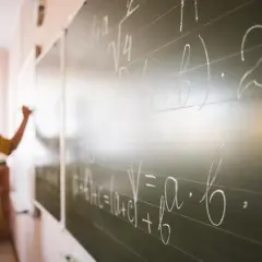 Nauczycielka pisze wzory matematyczne na tablicy. To art 20 karty nauczyciela, gdzie wiedza jest przekazywana.