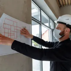 Mężczyzna w kasku i masce analizuje projekt budowlany. Dbałość o szczegóły, jak podczas studiów BHP, zapewnia bezpieczeństwo.