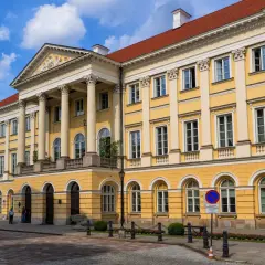 Majestatyczny żółty budynek z kolumnami, jeden z wielu uniwersytetów w Polsce, z czerwonym dachem i błękitnym niebem.