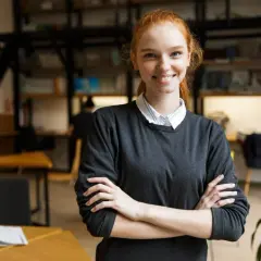 Uśmiechnięta studentka filologii hiszpańskiej z rudymi włosami, w bibliotece z książkami w tle.
