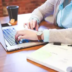 Osoba pracuje na laptopie, obok leży notatnik i długopis. Różne rodzaje wykształcenia można zdobywać w ten sposób.