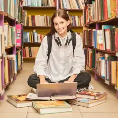 Uczennica z laptopem wśród książek. Zastanawia się, ile wynosi stypendium szkolne za dobre wyniki w nauce.