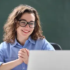 Uśmiechnięta nauczycielka w okularach przed laptopem, dyskutuje o nowelizacji Karty Nauczyciela.