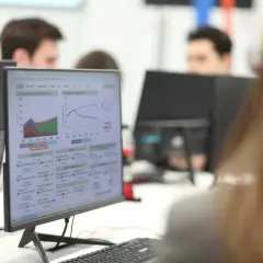 Studenci ekonomiczne analizują wykresy i dane na monitorach, pracując nad projektami.