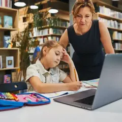 Dziewczynka z ołówkiem w dłoni, zamyślona nad zadaniem, przygotowuje podanie do szkoły średniej. Nauczycielka wspiera ją w bibliotece.