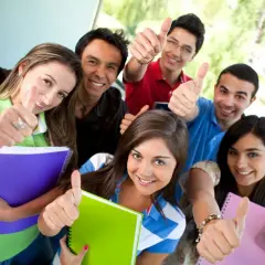 Uśmiechnięci studenci z notatnikami pokazują kciuki w górę, gotowi na studia stacjonarne.