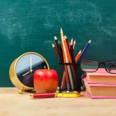Zegar, jabłko, lupa i przybory do pisania na tle tablicy. Czas na urlop bezpłatny nauczyciela.