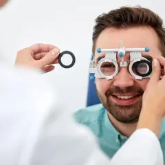 Badanie wzroku u optometrysty. Mężczyzna z uśmiechem na twarzy, któremu zakładane są soczewki próbne. To pierwszy krok, by dowiedzieć się, jak zostać optometrystą.