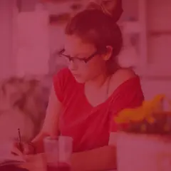 Dziewczyna w okularach pisze w zeszycie, zastanawiając się, ile kosztują studia zaoczne.