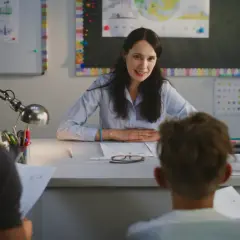 Nauczycielka z uśmiechem rozmawia z rodzicami ucznia, omawiając jego postępy. To przykład nadgodzin nauczycieli, poświęcających czas po lekcjach.