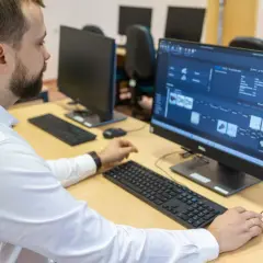 Mężczyzna w białej koszuli pracuje przy komputerze, analizując dane produkcyjne. To przykład nowoczesnego zarządzania i inżynierii produkcji.