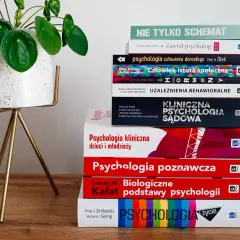 Stos książek do psychologii klinicznej studiów, w tym "Psychologia kliniczna dzieci i młodzieży" i "Psychologia sądowa", obok rośliny w doniczce.