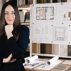 Młoda studentka architektury zamyślona nad projektami wnętrz, planszami z wizualizacjami i próbkami materiałów.