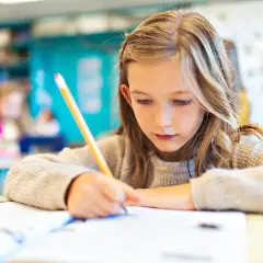 Dziewczynka skupiona na pisaniu w zeszycie. Czyżby zastanawiała się, od jakiej średniej jest 4?