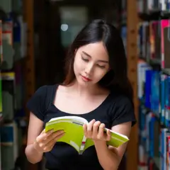 Młoda kobieta w bibliotece czyta książkę, zastanawiając się, od jakiej średniej jest stypendium.
