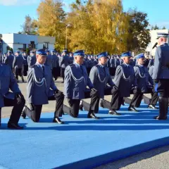 Uroczystość policyjna, policjanci w mundurach klęczą na niebieskim dywanie.