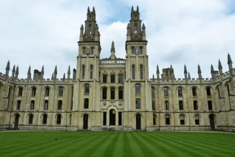 Imponująca architektura **Oxford uczelnia** z dwoma wieżami i zadbanym trawnikiem.