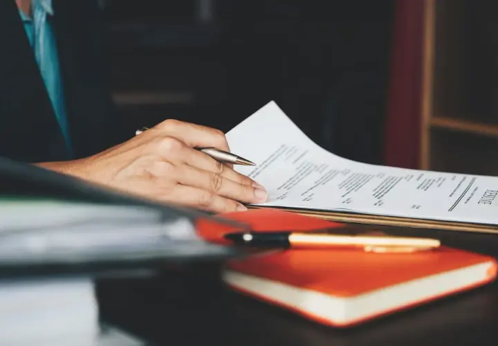 Ręka trzymająca długopis nad dokumentem z napisem "RESUME". To idealny moment na dopracowanie swojego CV po angielsku.