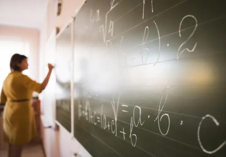 Nauczycielka pisze wzory matematyczne na tablicy. To art 20 karty nauczyciela, gdzie wiedza jest przekazywana.