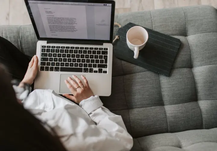 Scenarzysta pracuje nad nowym tekstem na laptopie, siedząc wygodnie na kanapie. Obok leży pusta filiżanka.