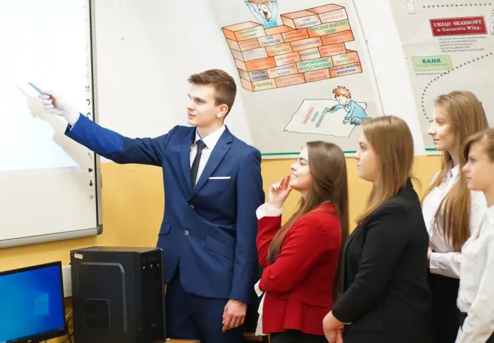 Młody technik ekonomista tłumaczy wykres na tablicy interaktywnej grupie uczniów.