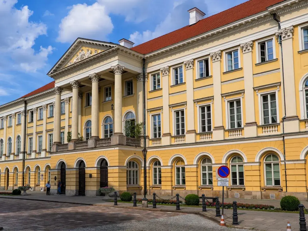 Majestatyczny żółty budynek z kolumnami, jeden z wielu uniwersytetów w Polsce, z czerwonym dachem i błękitnym niebem.