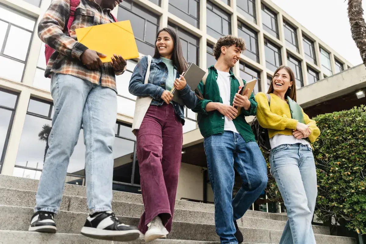 Grupa studentów schodzi po schodach, niosąc książki i teczki. Ich uśmiechy sugerują, że są gotowi na wyzwania, niczym w ramach obrony cywilnej.