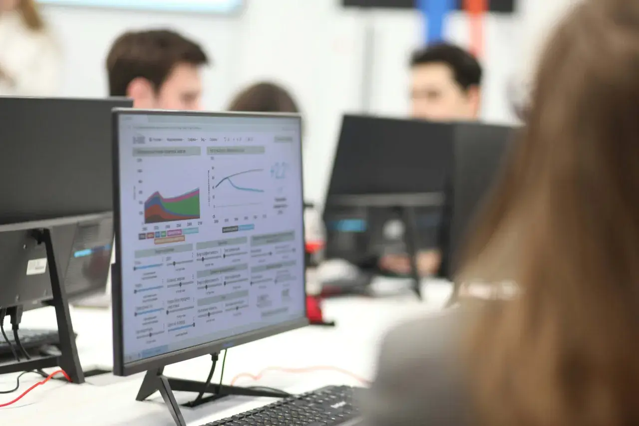 Studenci ekonomiczne analizują wykresy i dane na monitorach, pracując nad projektami.