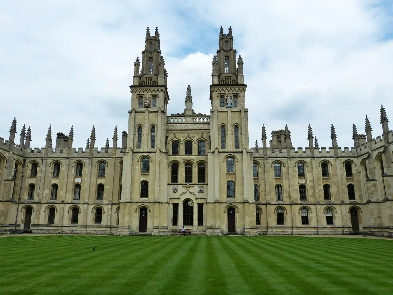 Imponująca architektura **Oxford uczelnia** z dwoma wieżami i zadbanym trawnikiem.