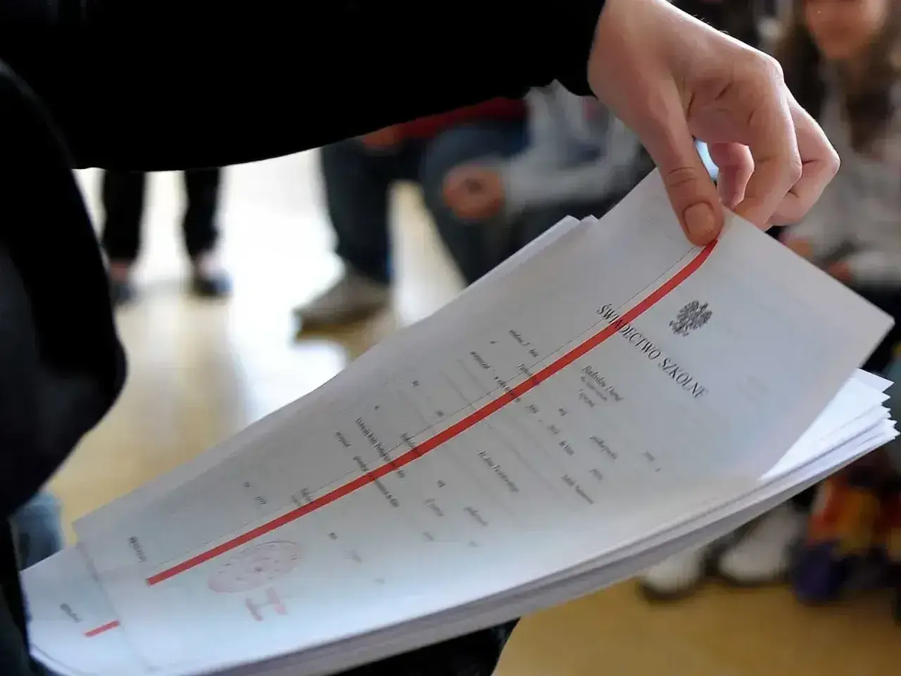 Dłoń trzyma stos świadectw szkolnych. Czy religia wlicza się do średniej? Ważne dokumenty edukacyjne.