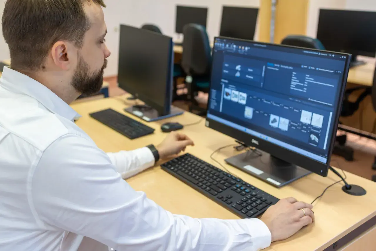 Mężczyzna w białej koszuli pracuje przy komputerze, analizując dane produkcyjne. To przykład nowoczesnego zarządzania i inżynierii produkcji.