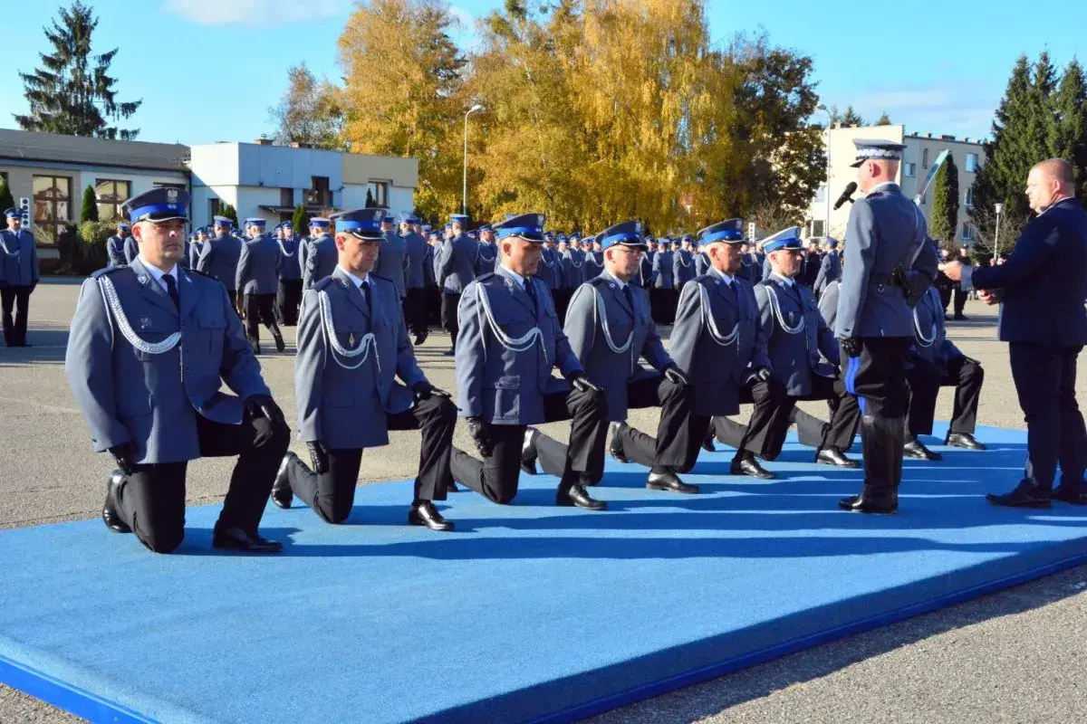 Uroczystość policyjna, policjanci w mundurach klęczą na niebieskim dywanie.