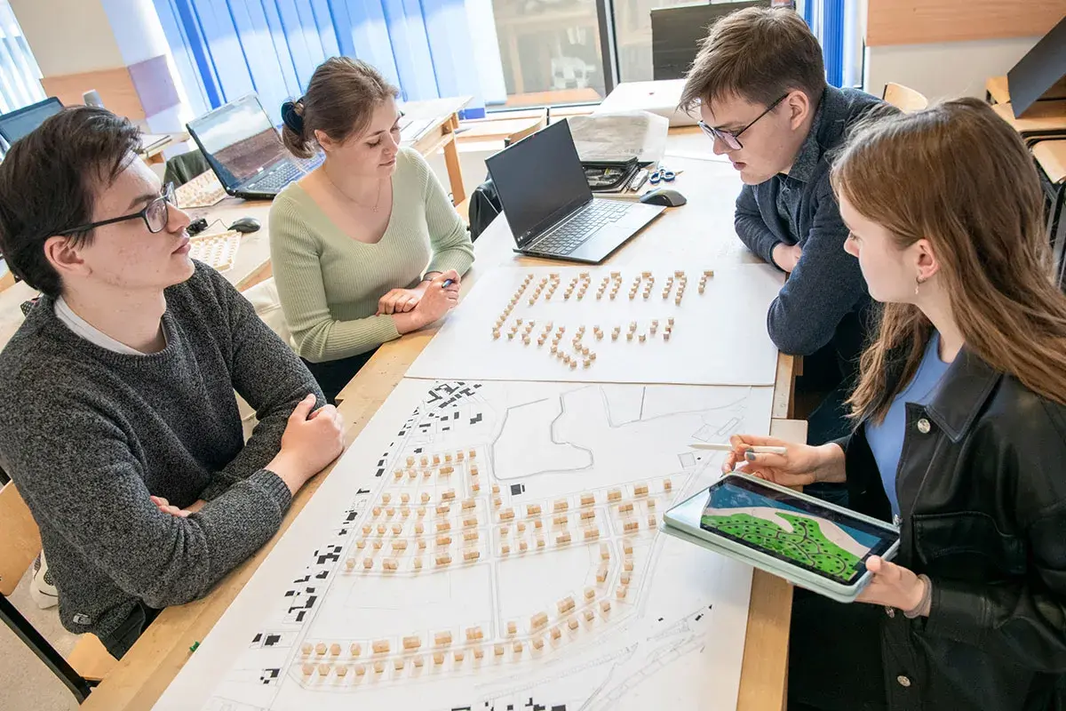 Studenci architektury analizują projekt urbanistyczny z makietą i planami.