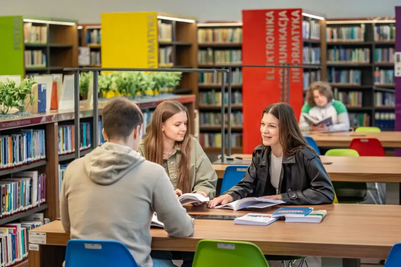 Studenci dyskutują o tym, ile trwa doktorat, w bibliotece pełnej książek.