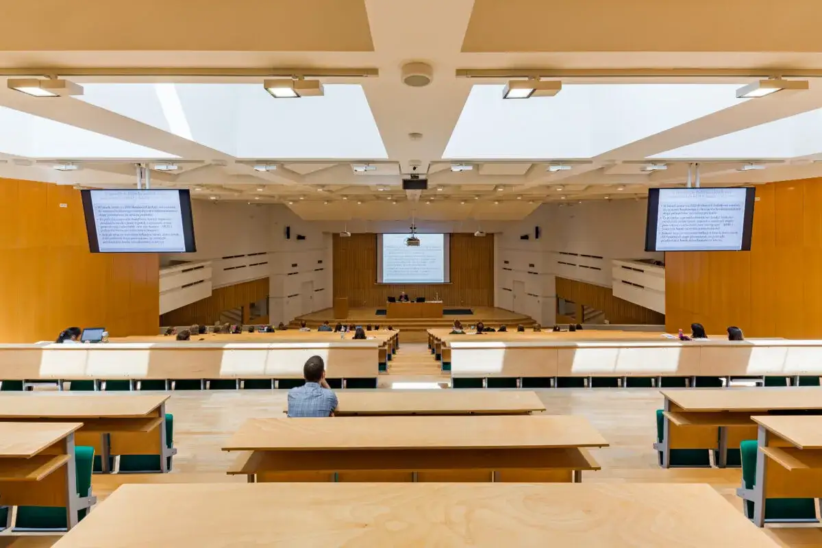 Nowoczesna sala wykładowa, idealna do zarządzania studiami. Widownia z drewnianymi ławkami i ekranami, gdzie studenci zdobywają wiedzę.