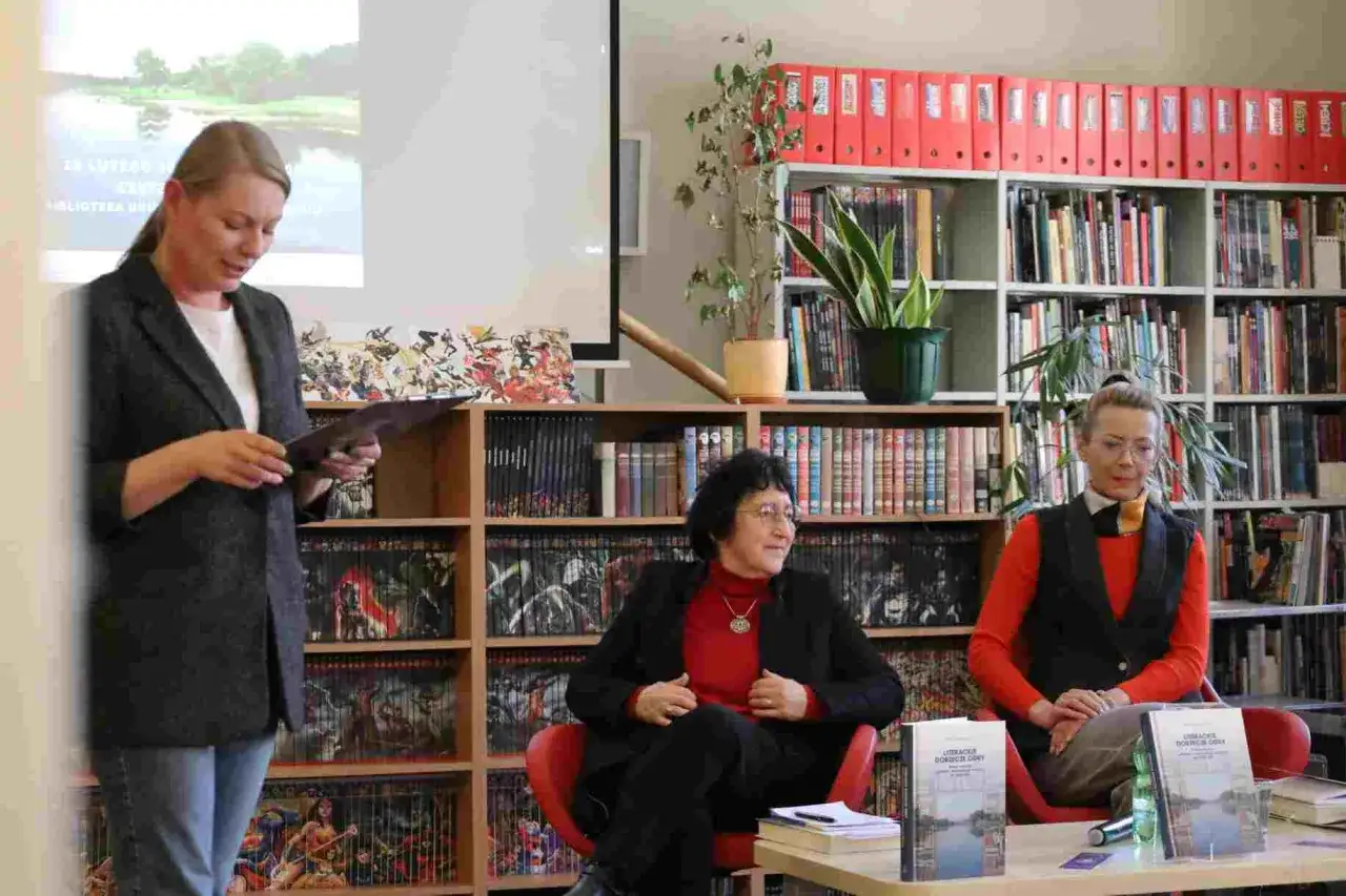 Spotkanie w bibliotece, gdzie dyskutuje się o studiach humanistycznych. Kobieta prezentuje książkę, siedzą dwie panie.