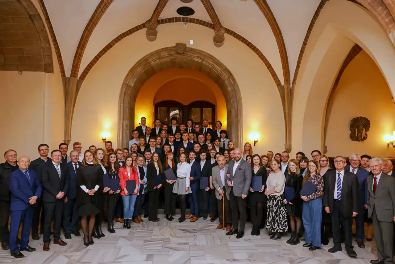 Grupa absolwentów studiów doktoranckich we Wrocławiu pozuje do wspólnego zdjęcia w zabytkowym wnętrzu.