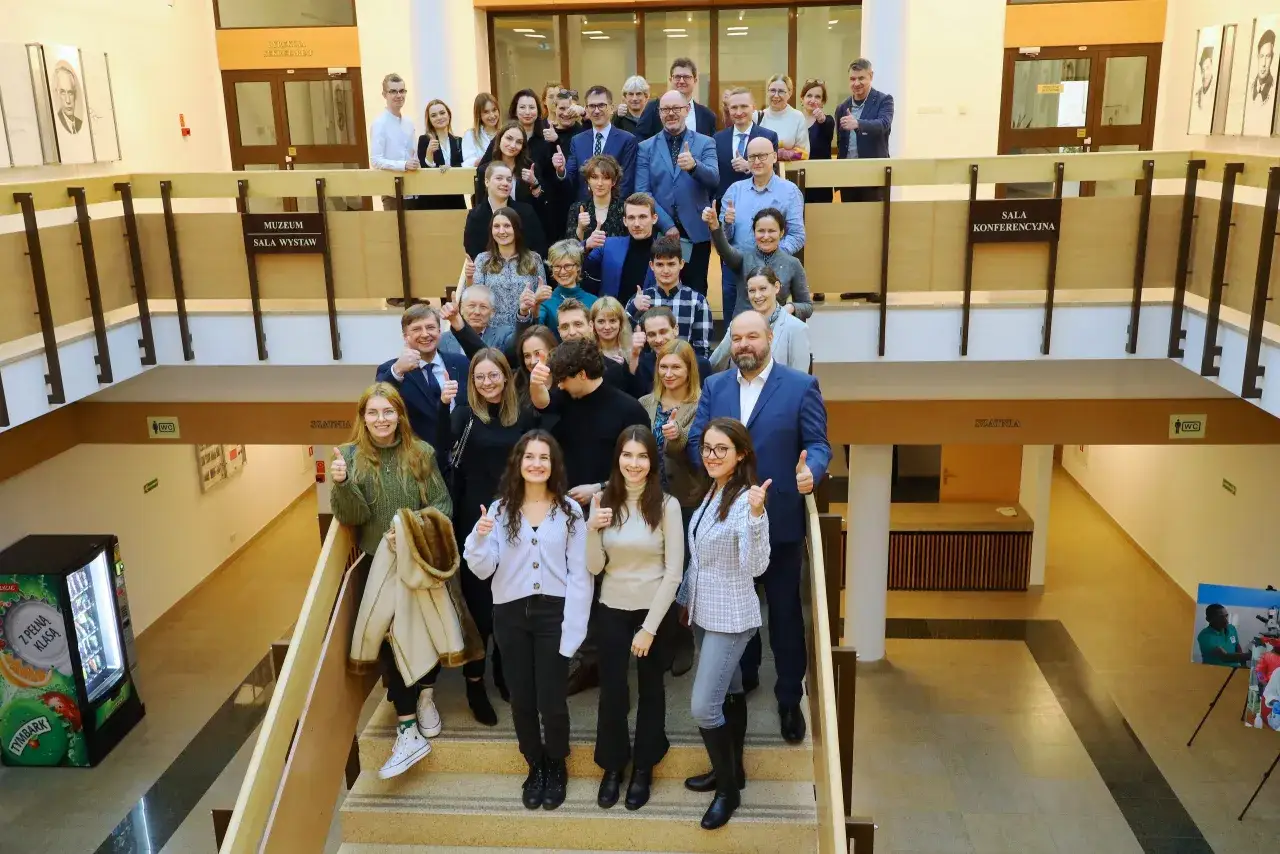 Grupa studentów architektury pozuje do zdjęcia na schodach. Wszyscy uśmiechnięci, pokazują kciuki w górę.