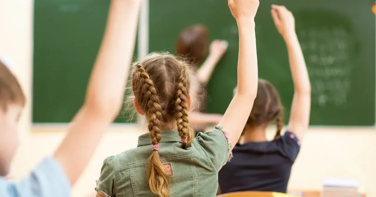 Uczniowie z podniesionymi rękami, zastanawiają się, czy zachowanie wlicza się do średniej. Nauczycielka pisze coś na tablicy.