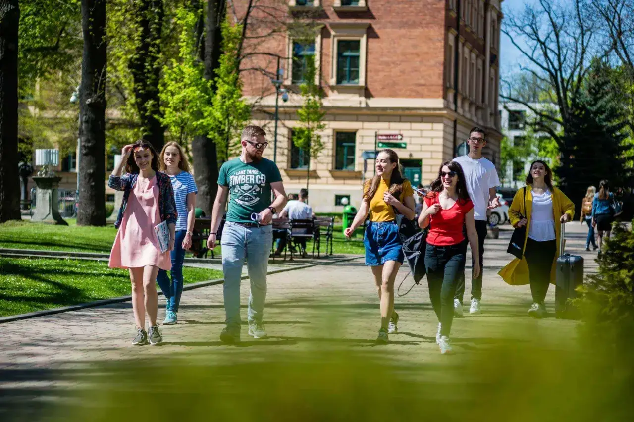 Grupa studentów idzie alejką w parku. Wszyscy wyglądają na szczęśliwych, jakby właśnie skończyli zajęcia. To typowy widok na wf na studiach.