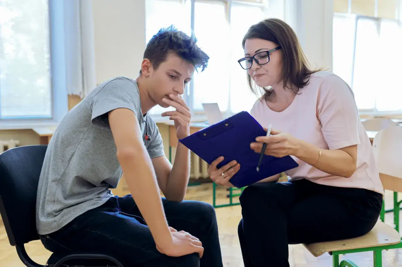 Chłopak w szarej koszulce słucha uważnie psycholog, która omawia wyniki diagnozy psychologicznej.