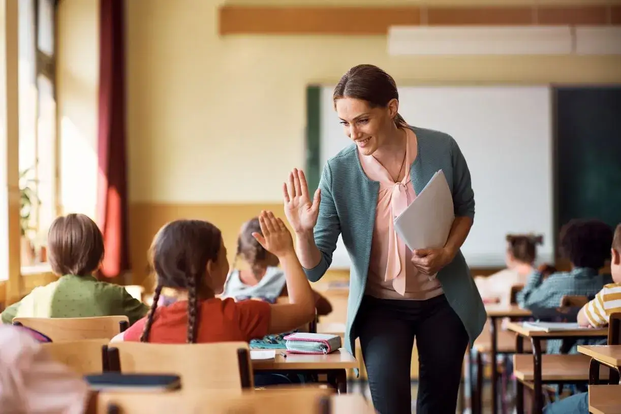 Nauczycielka daje piątkę uczennicy w klasie. To obrazek, który idealnie ilustruje, jak bon oświatowy może wspierać edukację i motywować uczniów.