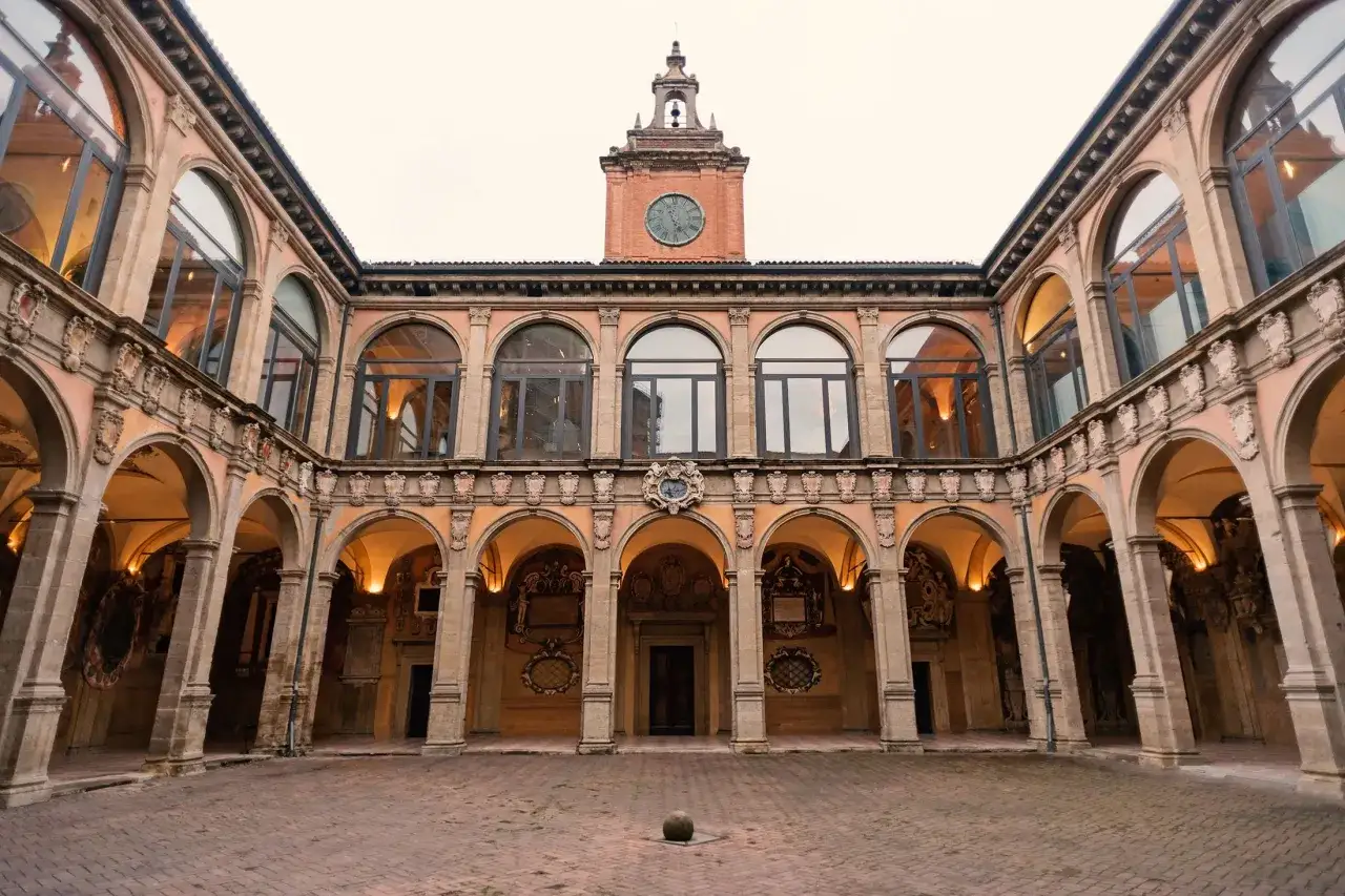 Dziedziniec Palazzo dell'Archiginnasio, siedziby najstarszego uniwersytetu na świecie, z arkadami i zegarem na wieży.