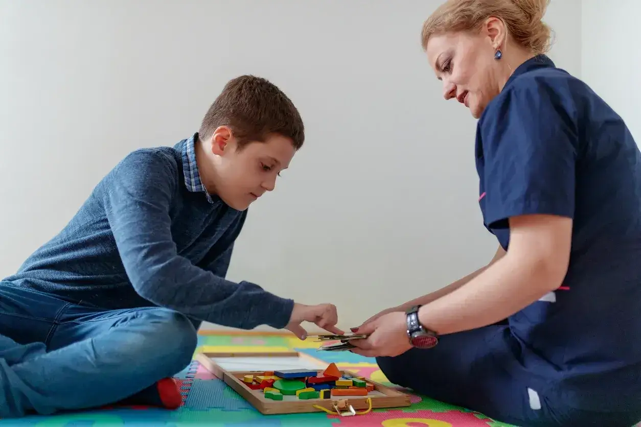 Chłopiec z terapeutką układa klocki. To przykład praktycznych zajęć podczas terapii pedagogicznej, studiów podyplomowych.