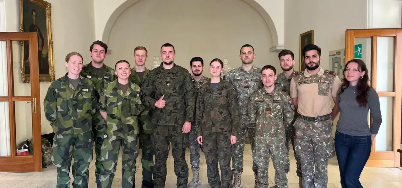 Grupa młodych ludzi w mundurach wojskowych, uczestnicy studiów wojskowych, pozuje do zdjęcia wewnątrz budynku.