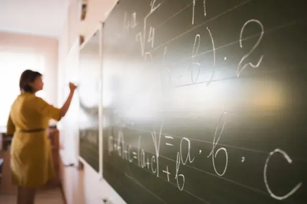 Nauczycielka pisze wzory matematyczne na tablicy. To art 20 karty nauczyciela, gdzie wiedza jest przekazywana.
